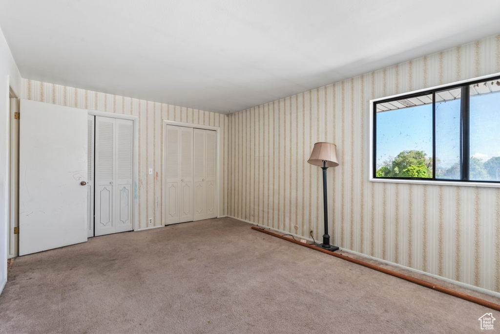 Unfurnished bedroom with multiple closets, carpet flooring, and wallpapered walls