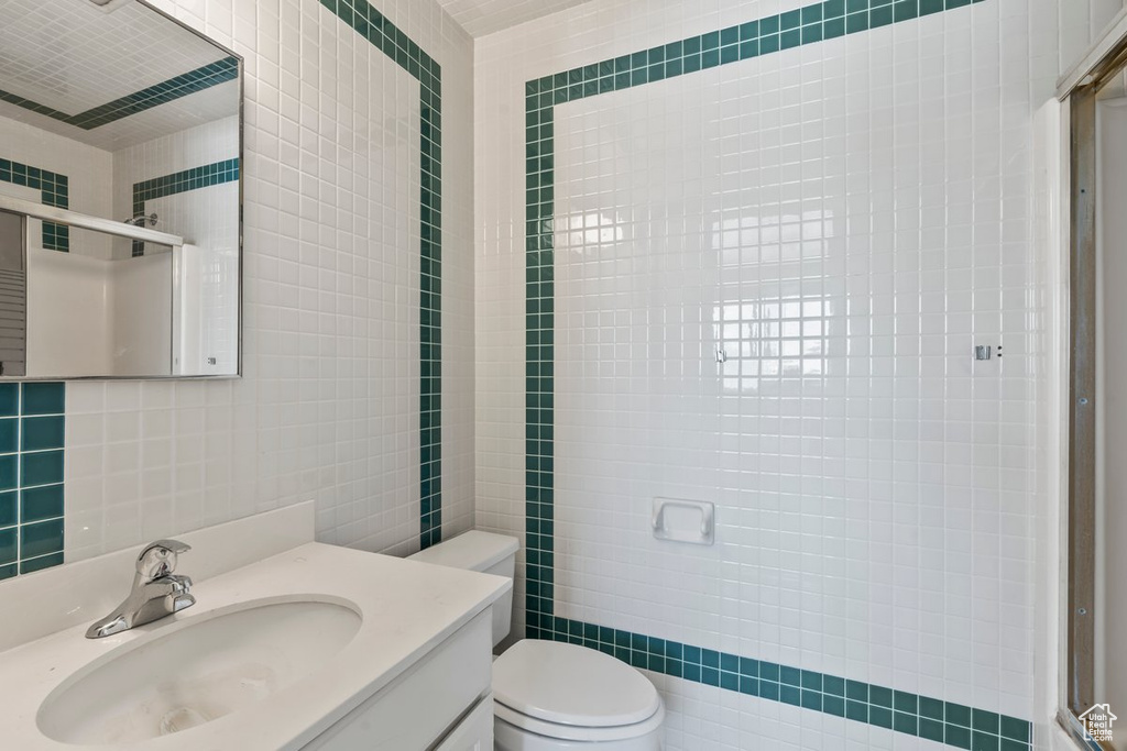 Bathroom with a shower with shower door, tile walls, vanity, and toilet