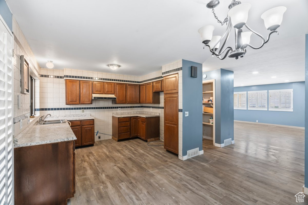 Kitchen with under cabinet range hood, wood finished floors, a notable chandelier, and brown cabinets