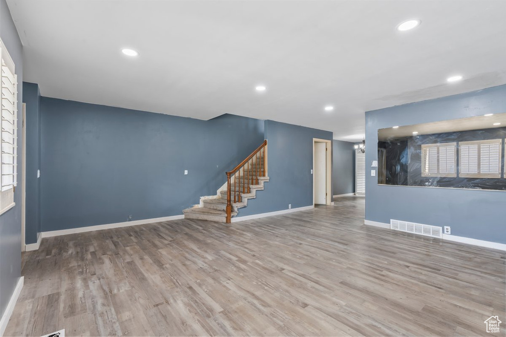 Unfurnished living room featuring baseboards, stairway, visible vents, and wood finished floors