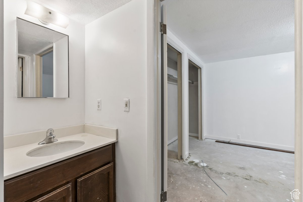Bathroom with unfinished concrete floors, vanity, and a textured ceiling