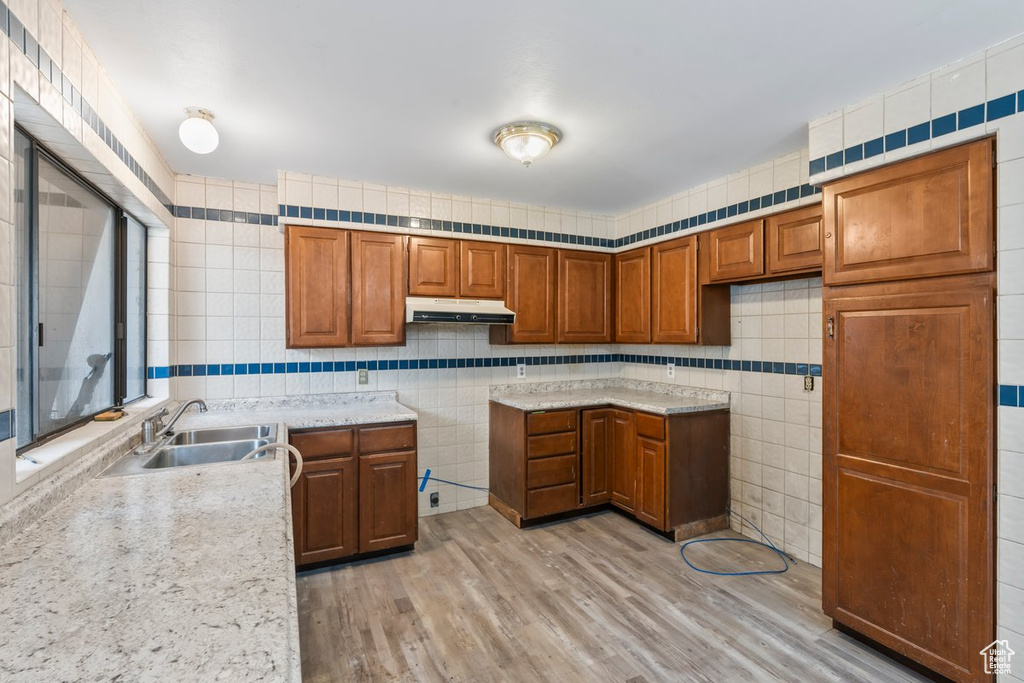 Kitchen with tile walls, brown cabinets, a sink, and under cabinet range hood