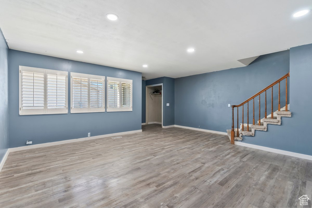 Unfurnished living room with recessed lighting, wood finished floors, baseboards, and stairs