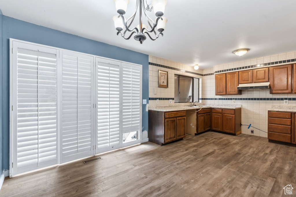Kitchen with an inviting chandelier, brown cabinets, visible vents, under cabinet range hood, and dishwasher