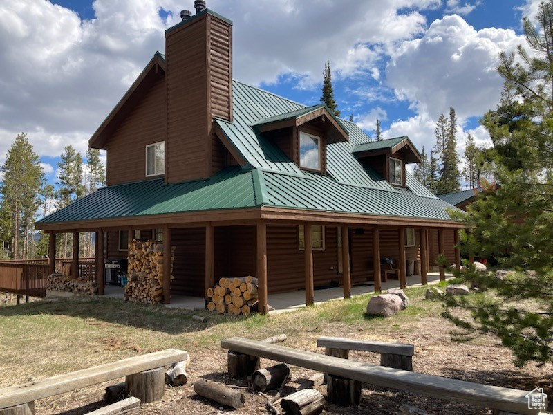 Back of house with a patio, log veneer siding, a chimney, metal roof, and a standing seam roof