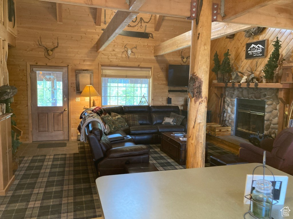 Living room featuring wooden walls, a fireplace, a healthy amount of sunlight, and vaulted ceiling with beams