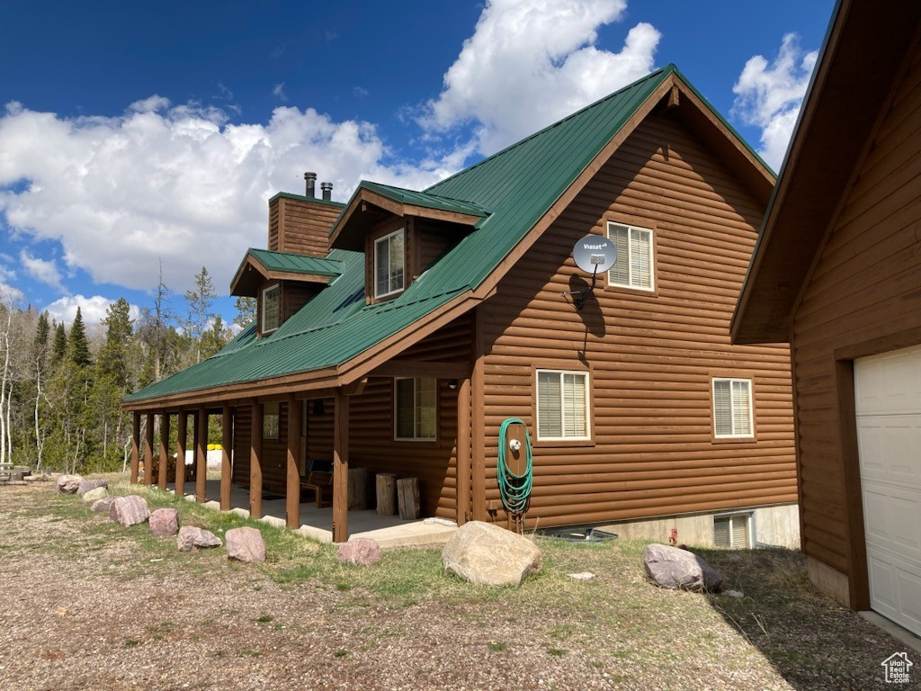 View of property exterior featuring a patio area, a garage, metal roof, a chimney, and log veneer siding