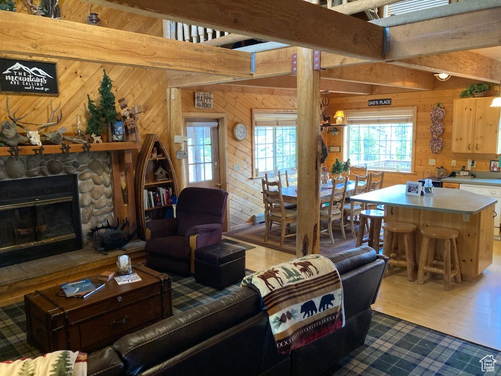 Living room with a stone fireplace, wooden walls, wood finished floors, and beamed ceiling