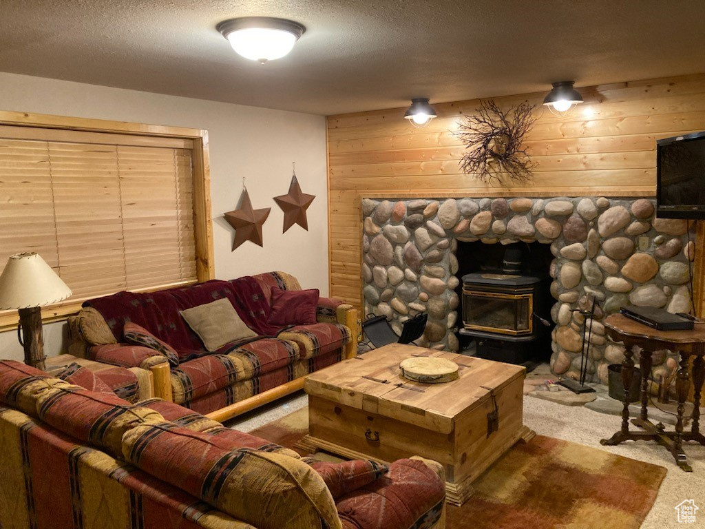 Living area with carpet flooring, a textured ceiling, wood walls, and a wood stove