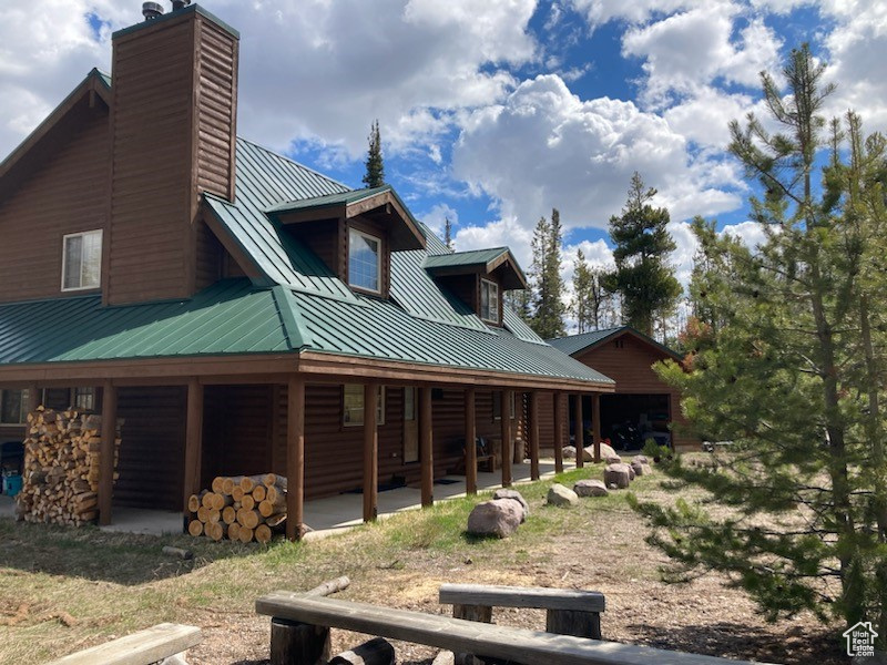 Back of property with a chimney, a standing seam roof, log veneer siding, metal roof, and a garage
