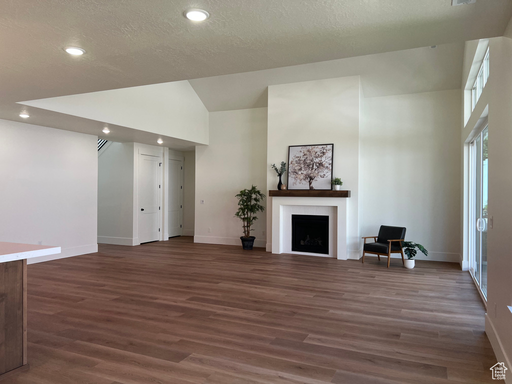 Unfurnished living room with a fireplace, wood finished floors, recessed lighting, a textured ceiling, and high vaulted ceiling