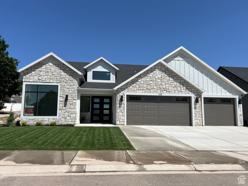 View of front of house featuring stone siding, a garage, a front lawn, concrete driveway, and board and batten siding