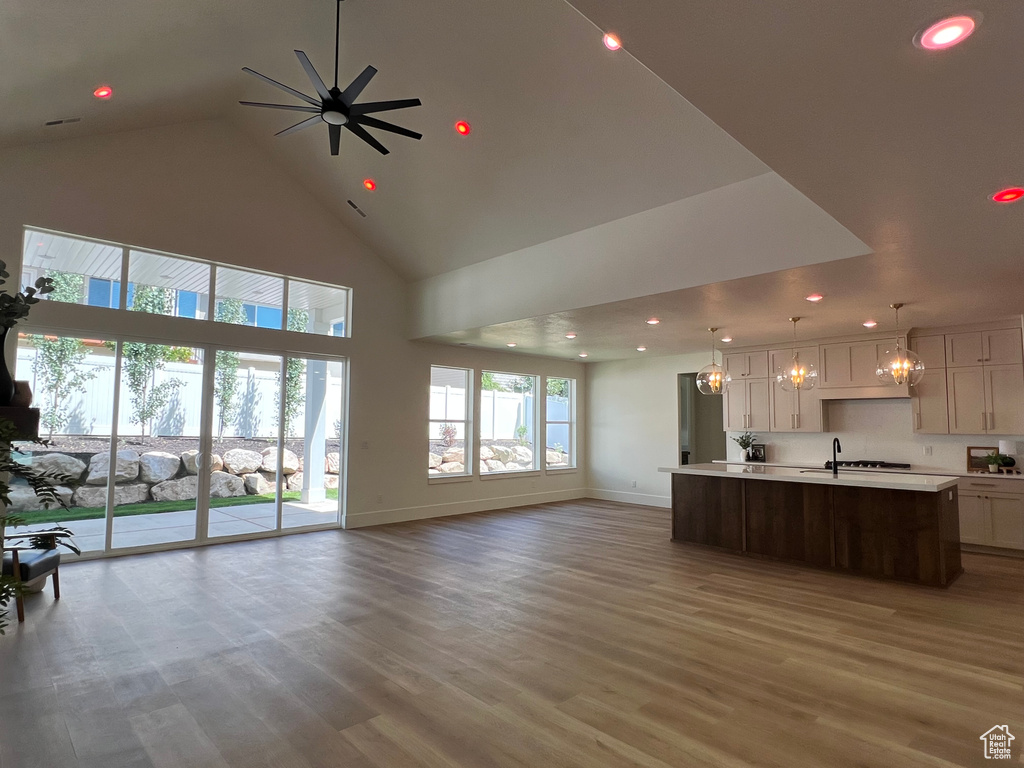 Unfurnished living room with high vaulted ceiling, recessed lighting, light wood-style flooring, a ceiling fan, and a chandelier