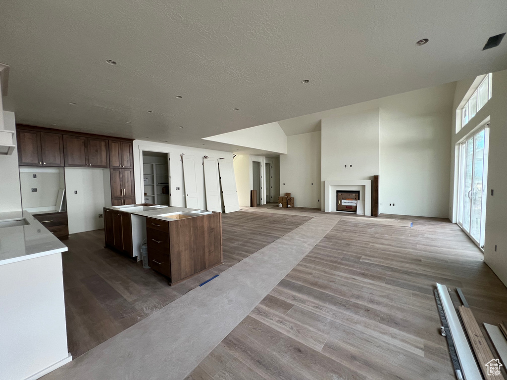 Kitchen with dark brown cabinets, wood finished floors, a fireplace, a textured ceiling, and a kitchen island