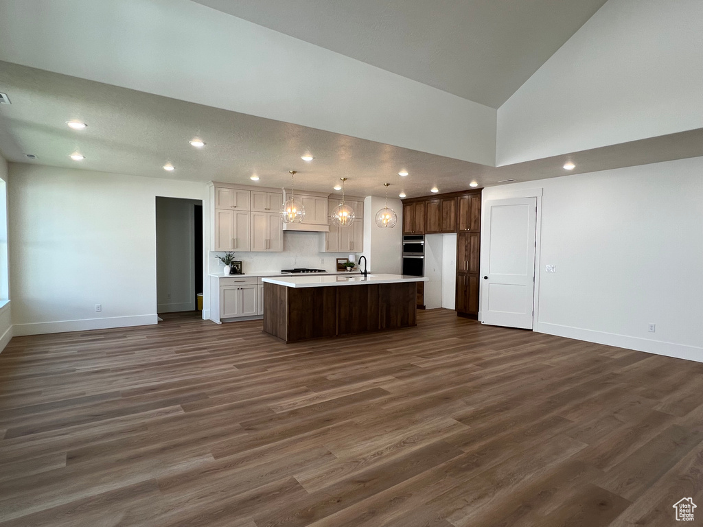 Kitchen with open floor plan, light countertops, a center island with sink, dark wood-style floors, and recessed lighting