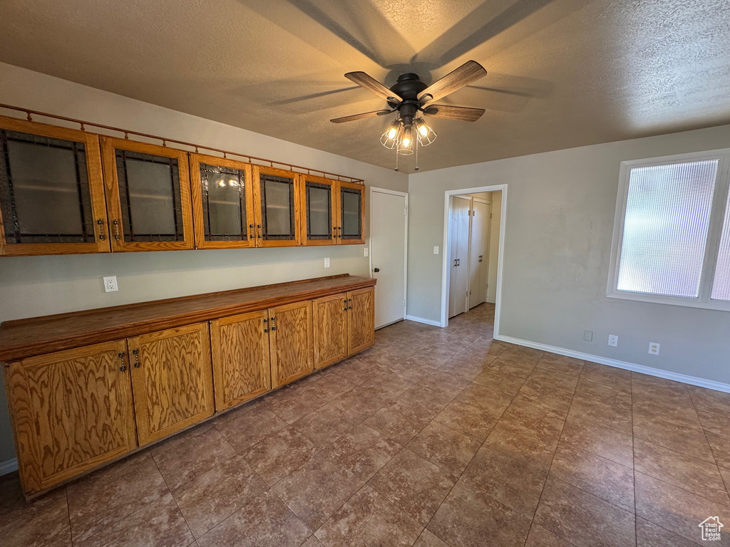 Kitchen featuring a ceiling fan, a textured ceiling, glass insert cabinets, brown cabinetry, and baseboards