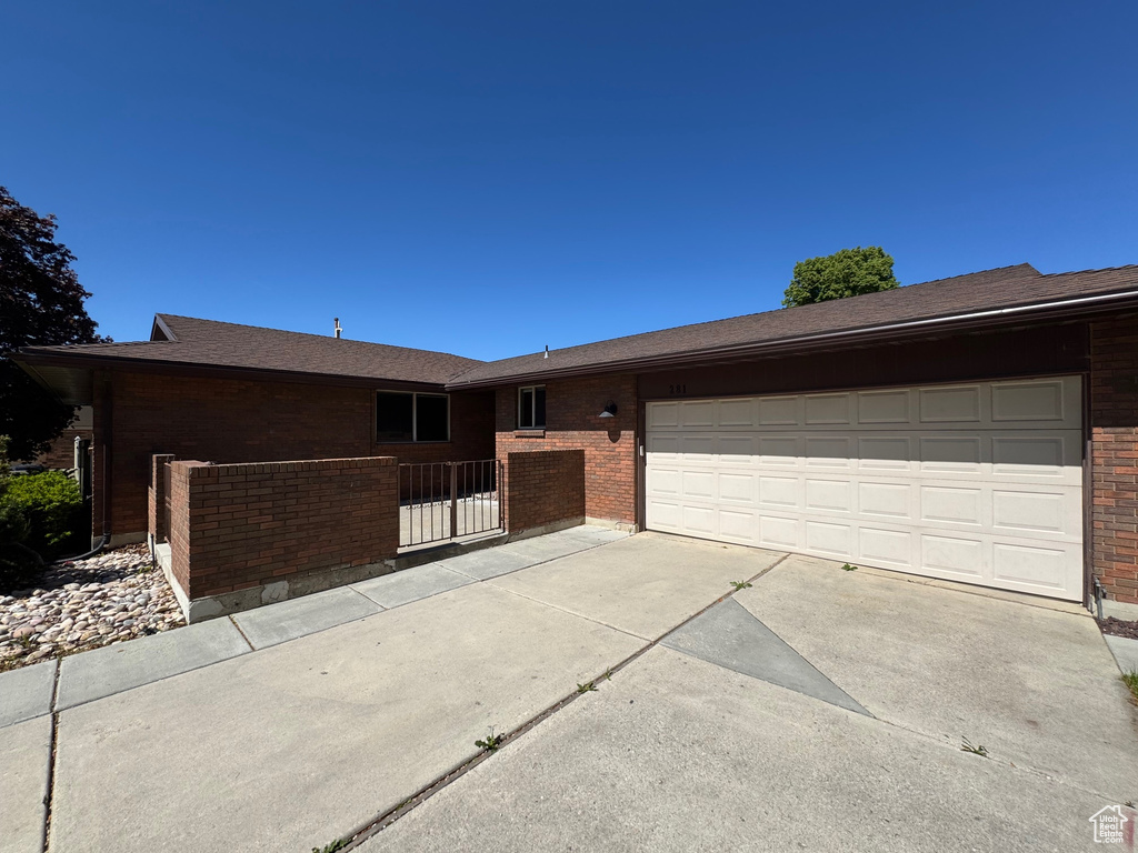 Ranch-style house featuring concrete driveway, brick siding, an attached garage, and fence