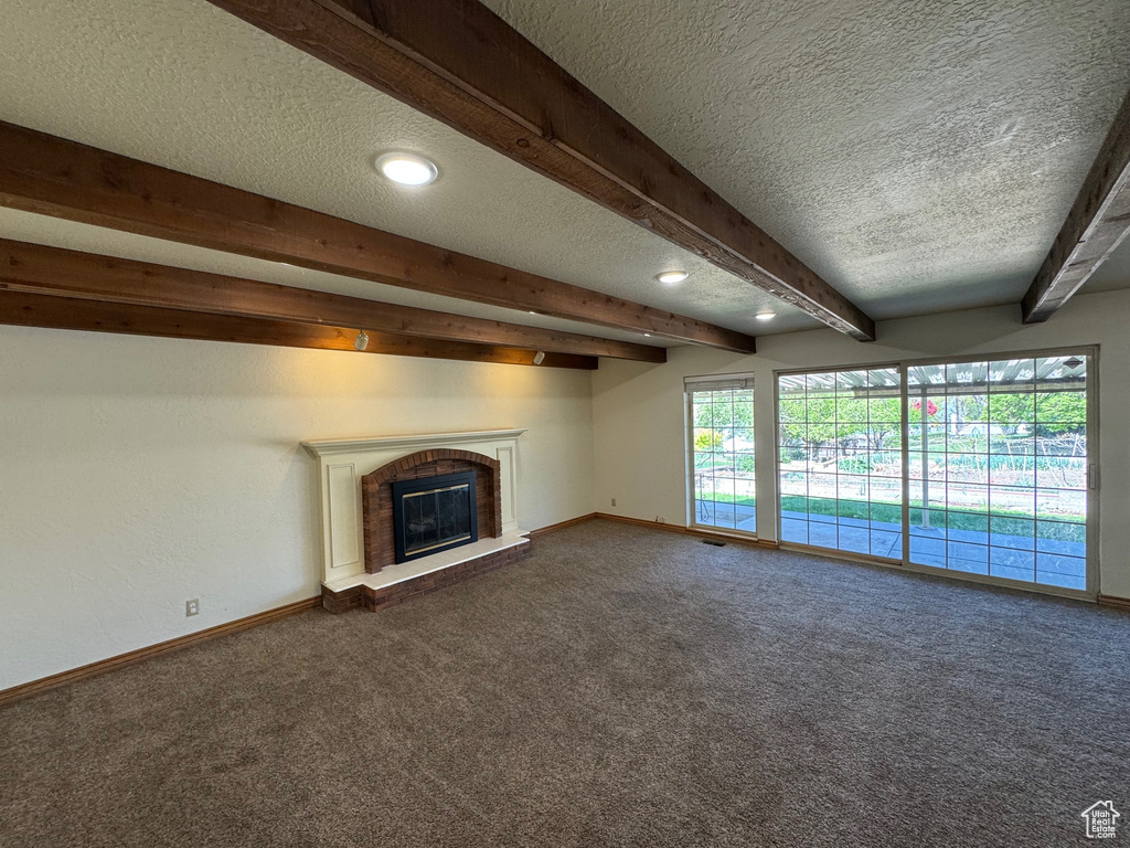 Unfurnished living room featuring a fireplace, a textured ceiling, baseboards, beamed ceiling, and dark colored carpet