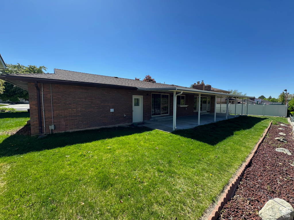 Rear view of house with a chimney, fence, a yard, brick siding, and a patio area