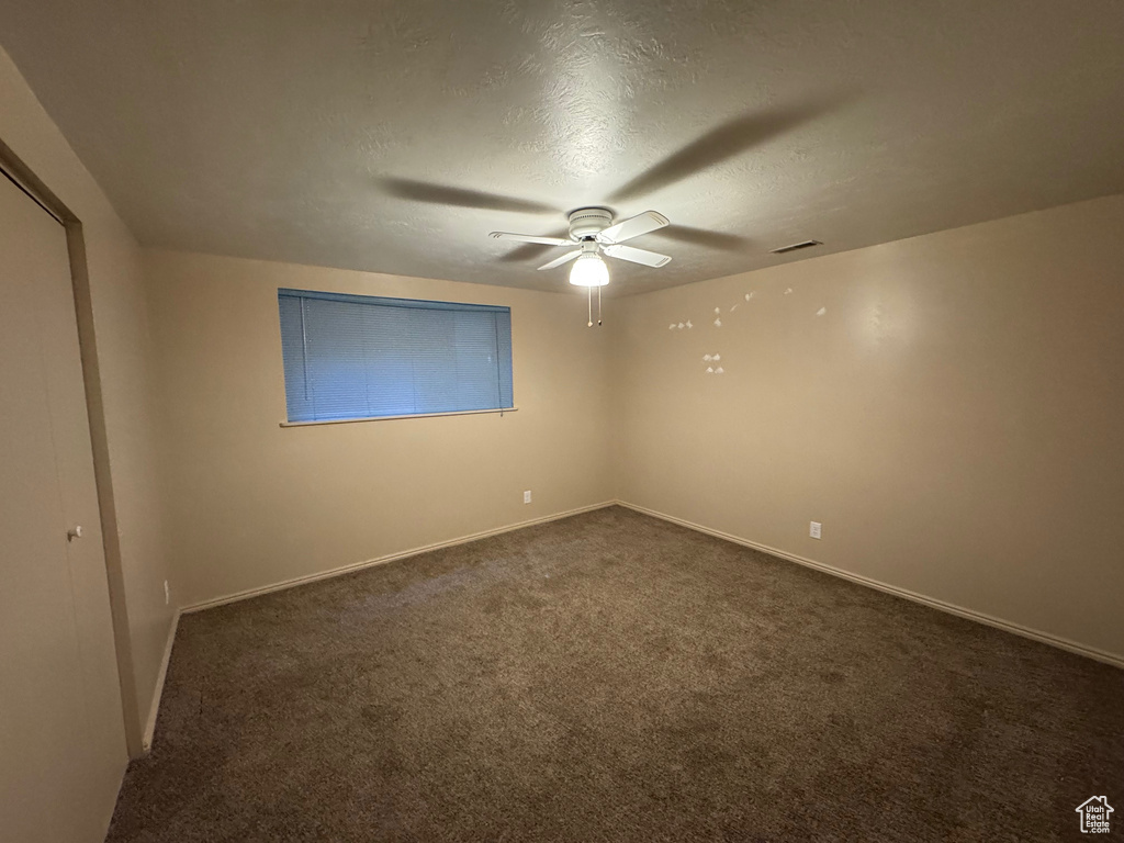 Unfurnished room featuring ceiling fan, a textured ceiling, baseboards, and dark carpet
