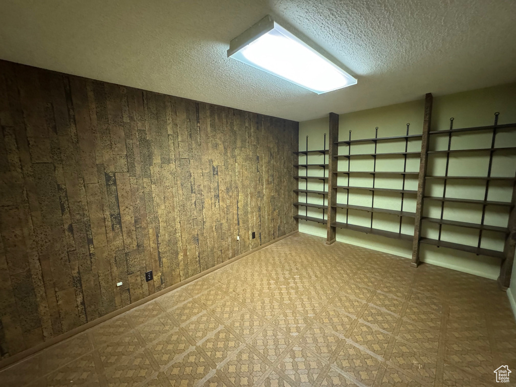 Basement featuring tile patterned floors, wood walls, and a textured ceiling