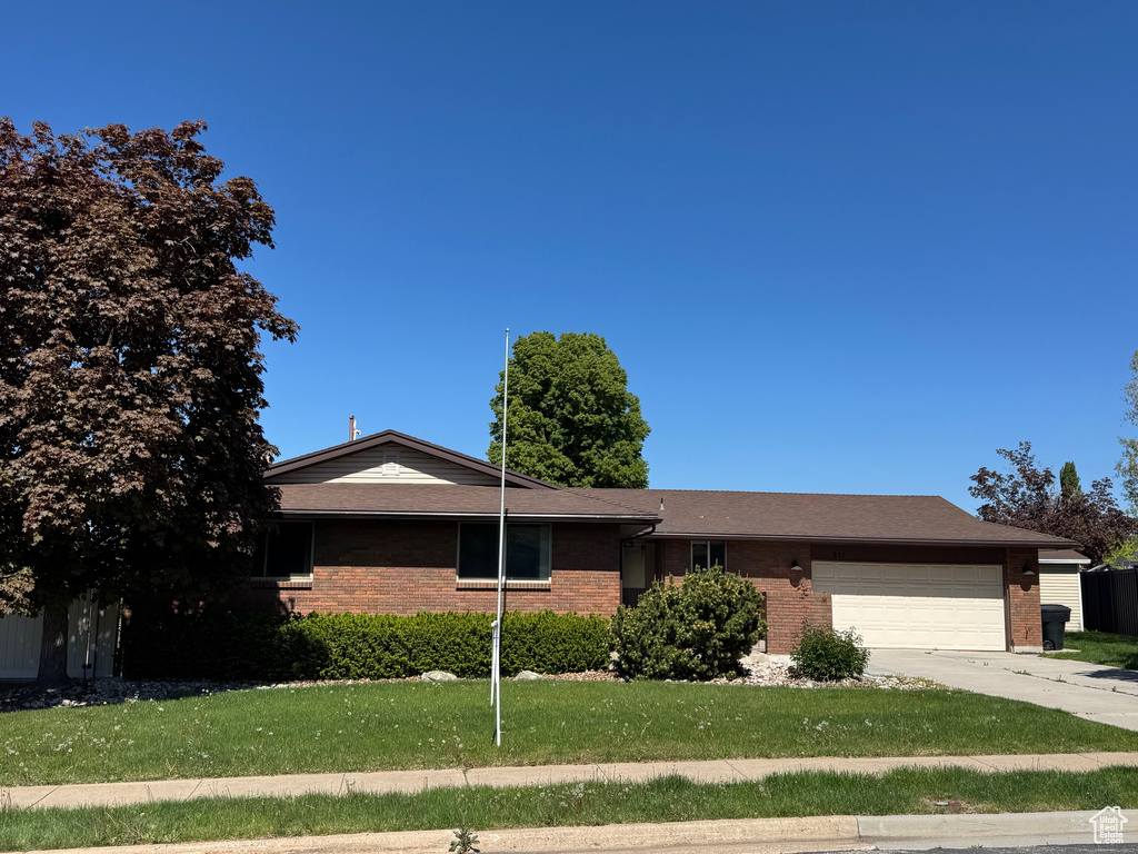 Ranch-style home with concrete driveway, a front yard, brick siding, and a garage