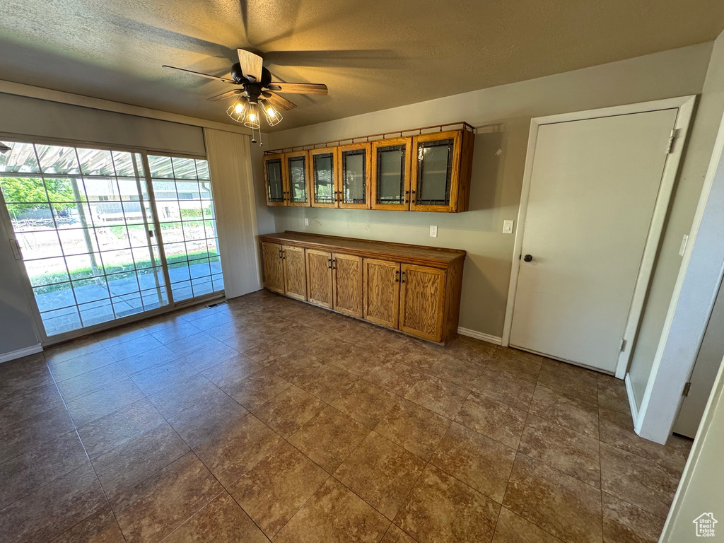 Kitchen with brown cabinetry, a textured ceiling, a ceiling fan, glass insert cabinets, and baseboards