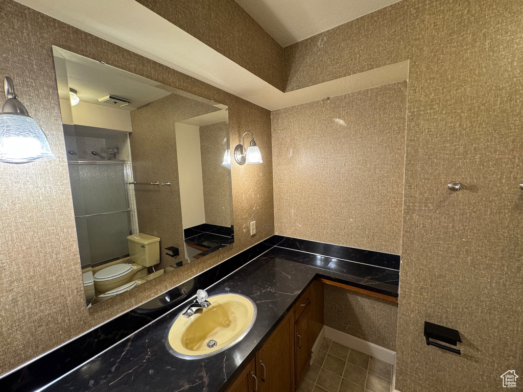 Bathroom with toilet, a shower with door, tile patterned flooring, and vanity
