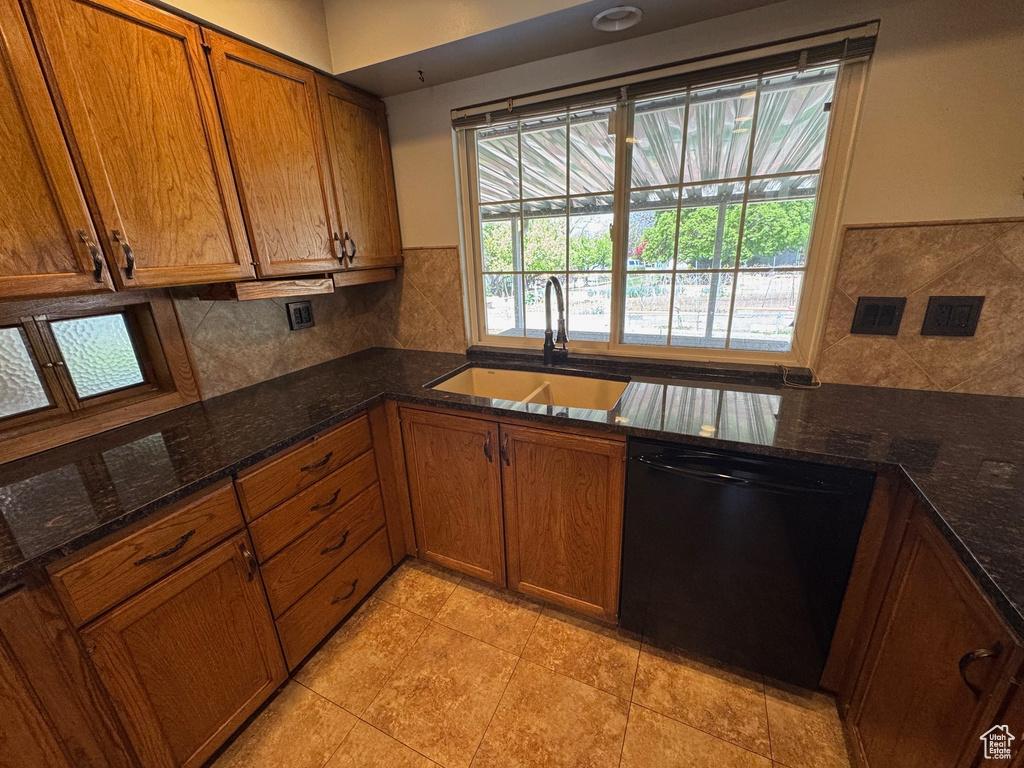 Kitchen with brown cabinetry, backsplash, black dishwasher, and a sink