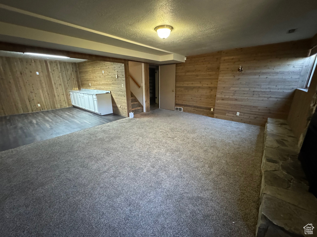 Unfurnished living room featuring a textured ceiling, visible vents, wood walls, stairway, and carpet floors
