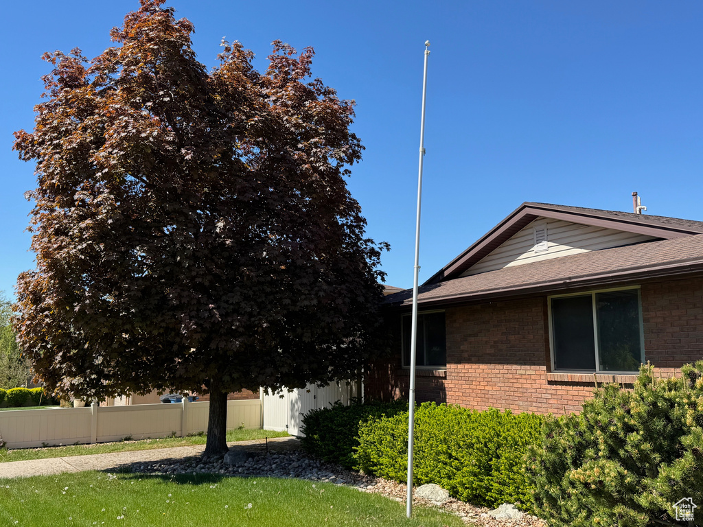 View of side of home featuring roof with shingles, brick siding, and fence