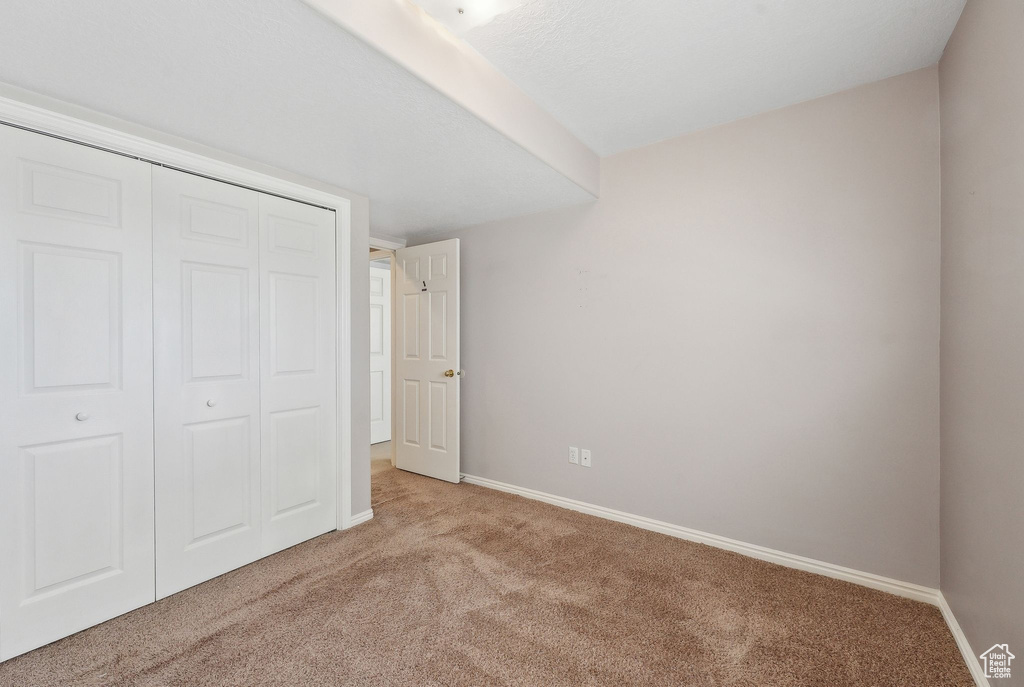 Unfurnished bedroom with light colored carpet, baseboards, and a closet