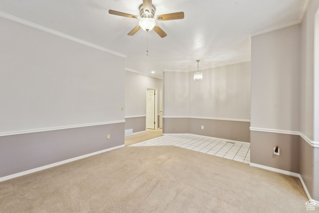 Carpeted spare room with ornamental molding, ceiling fan with notable chandelier, and baseboards