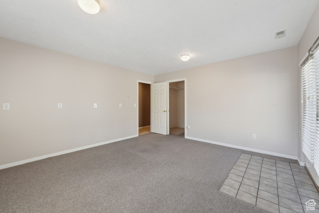 Unfurnished bedroom featuring a walk in closet, light carpet, baseboards, and visible vents