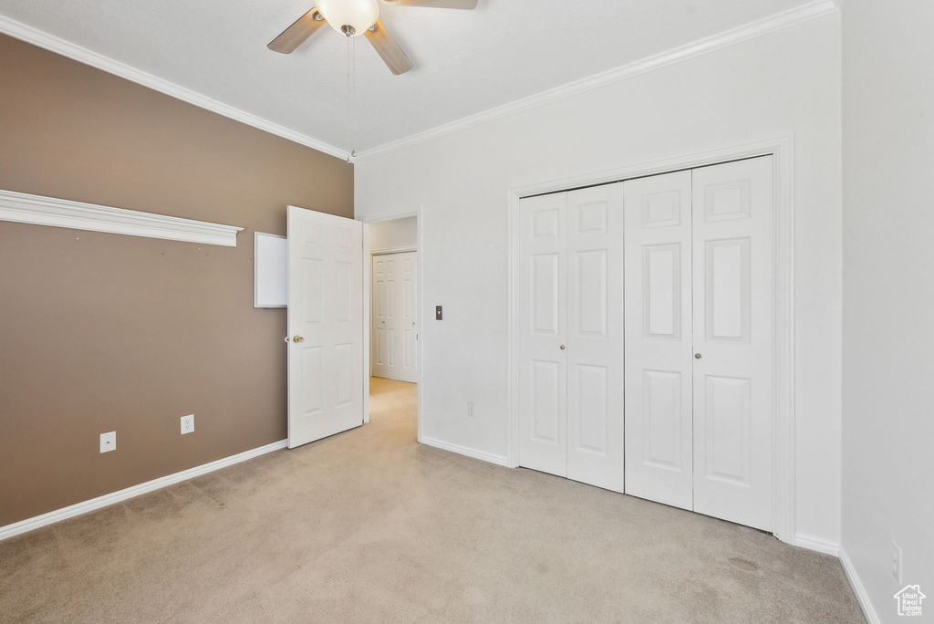 Unfurnished bedroom featuring ornamental molding, light carpet, baseboards, and a closet