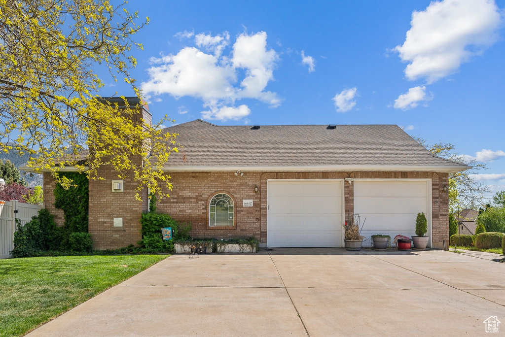 View of front facade with driveway, brick siding, a garage, a shingled roof, and a front yard