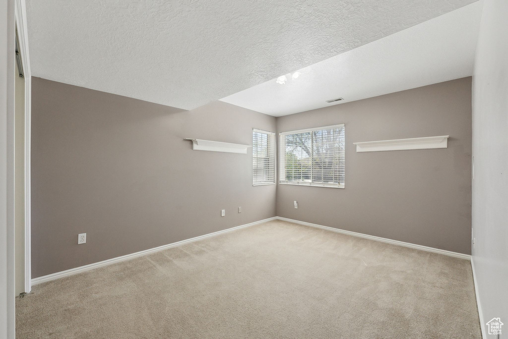 Spare room featuring a textured ceiling, visible vents, baseboards, and carpet floors