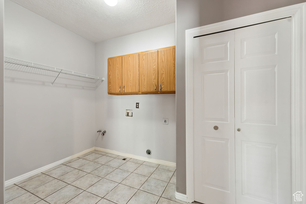 Clothes washing area with cabinet space, hookup for an electric dryer, light tile patterned floors, washer hookup, and baseboards
