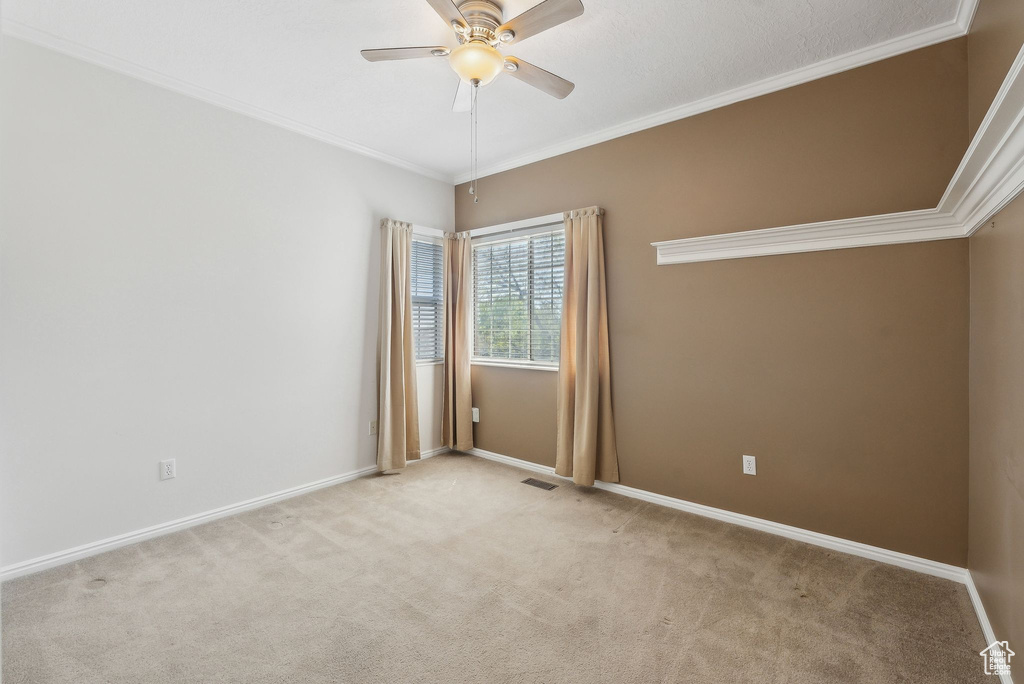Empty room featuring baseboards, light carpet, crown molding, and ceiling fan