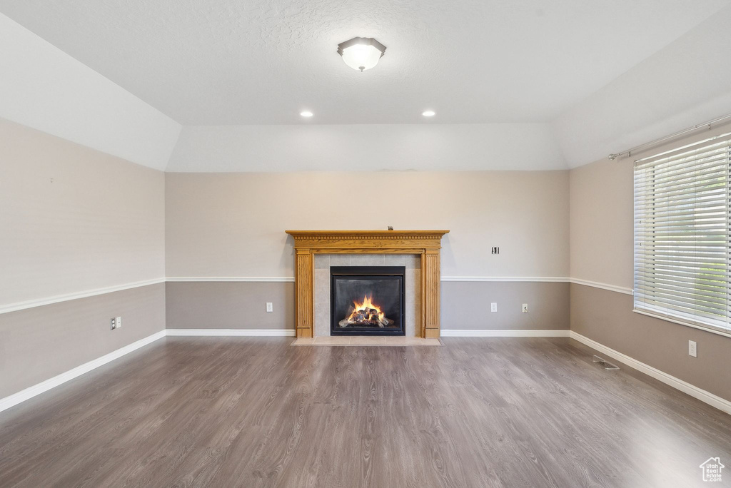 Unfurnished living room featuring wood finished floors, a fireplace, baseboards, lofted ceiling, and recessed lighting