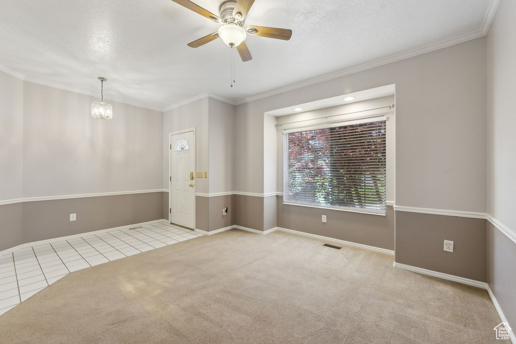 Carpeted empty room with baseboards, tile patterned flooring, crown molding, and ceiling fan with notable chandelier