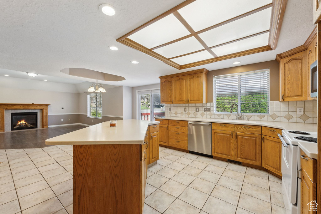 Kitchen featuring decorative backsplash, a center island, light tile patterned floors, a glass covered fireplace, and appliances with stainless steel finishes