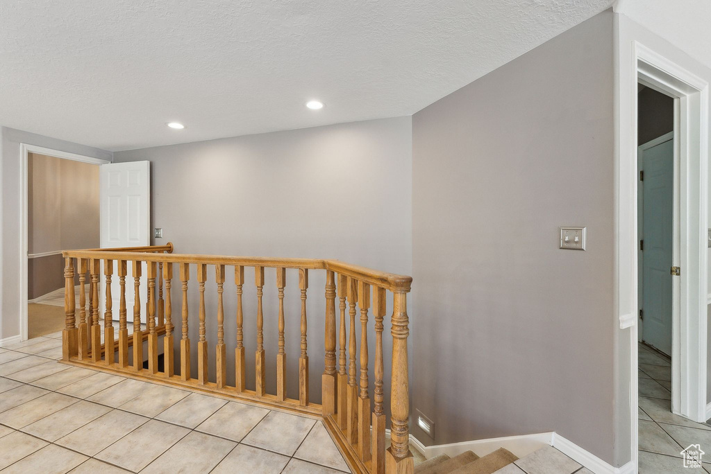 Interior space with a textured ceiling, an upstairs landing, light tile patterned flooring, and recessed lighting