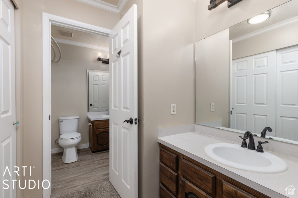 Bathroom with toilet, ornamental molding, visible vents, vanity, and wood finished floors