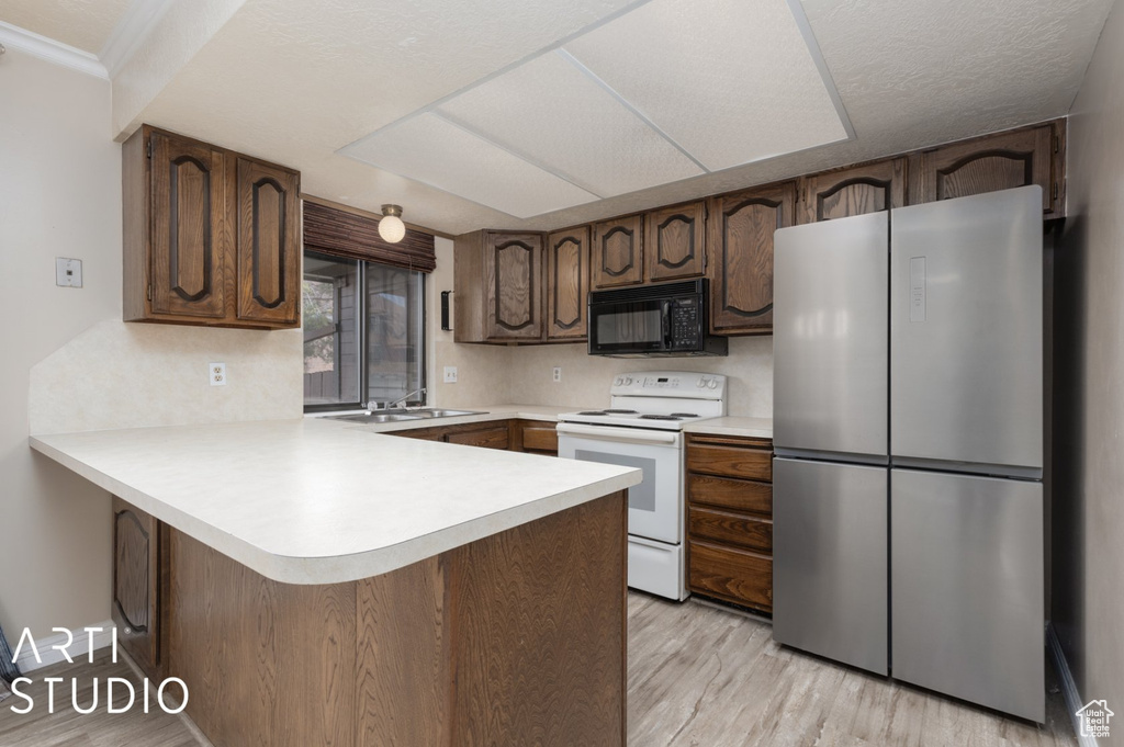 Kitchen with a peninsula, freestanding refrigerator, black microwave, light countertops, and white electric range