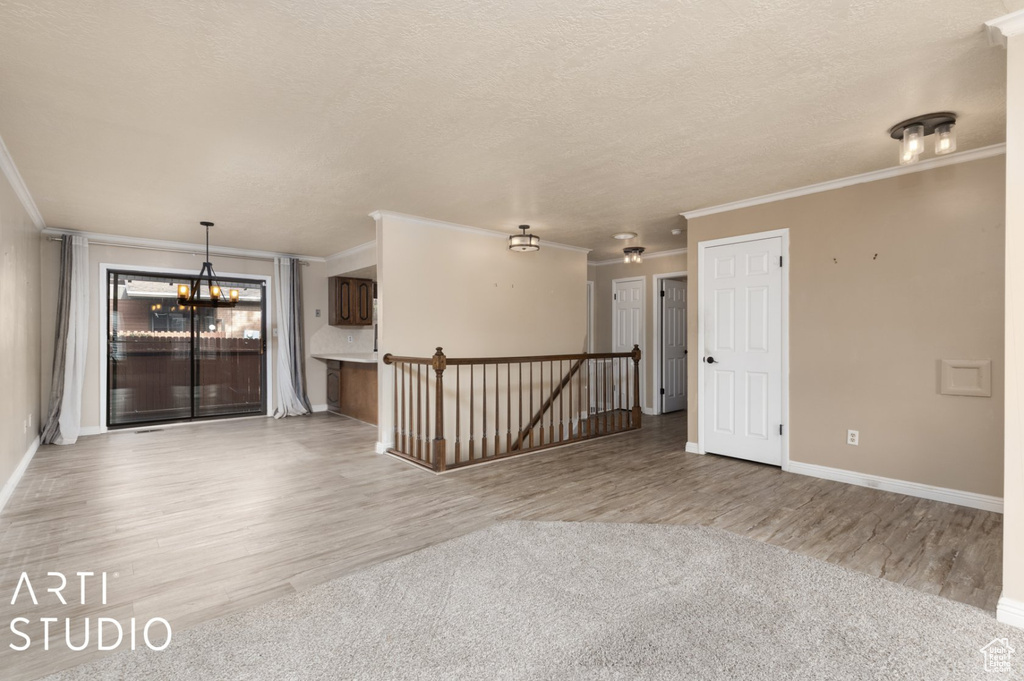 Unfurnished room with wood finished floors, a textured ceiling, baseboards, crown molding, and a notable chandelier