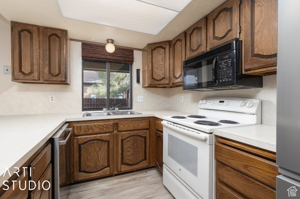 Kitchen with white electric stove, a sink, black microwave, light countertops, and light wood-type flooring