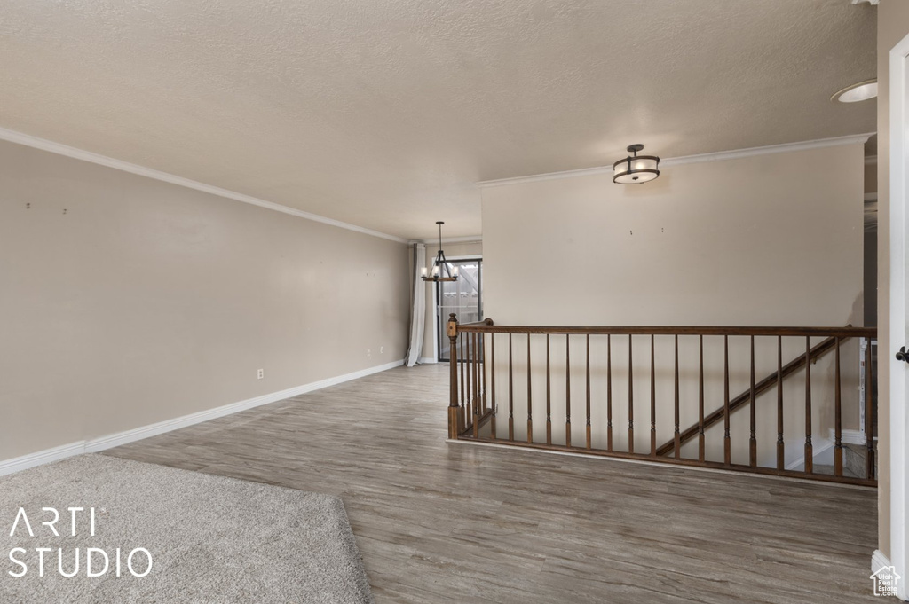 Spare room featuring a notable chandelier, a textured ceiling, baseboards, ornamental molding, and wood finished floors
