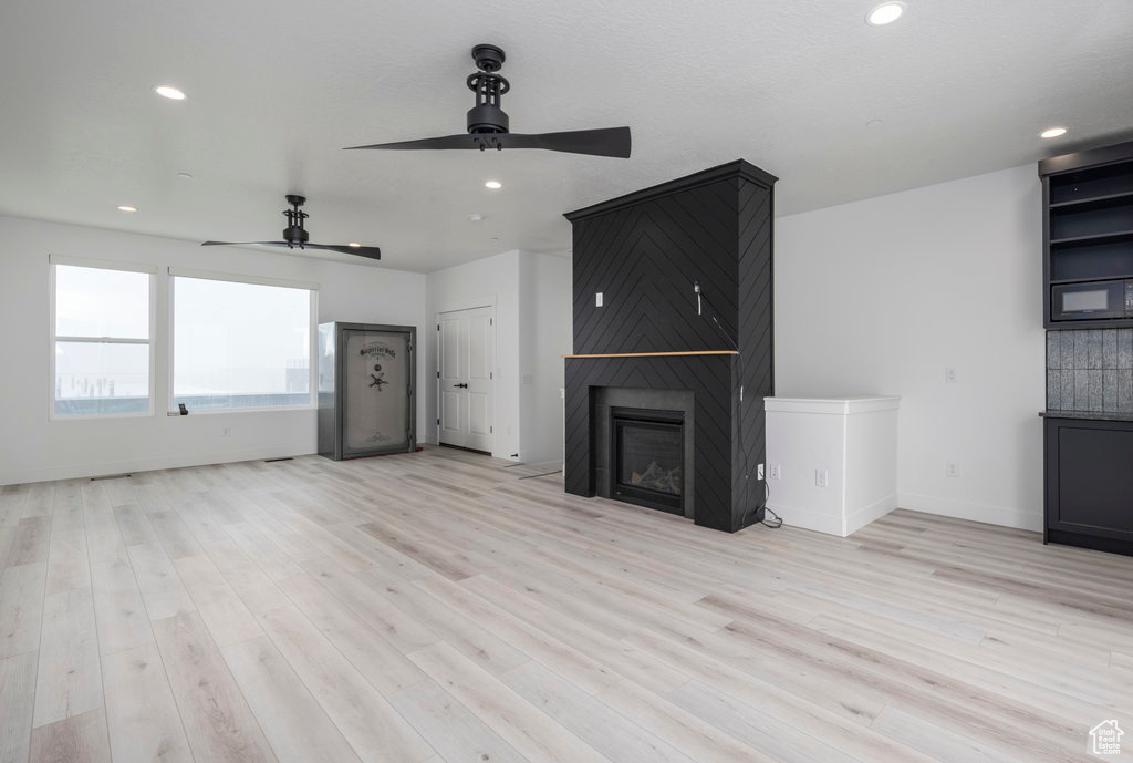 Unfurnished living room featuring a large fireplace, a ceiling fan, light wood finished floors, and recessed lighting