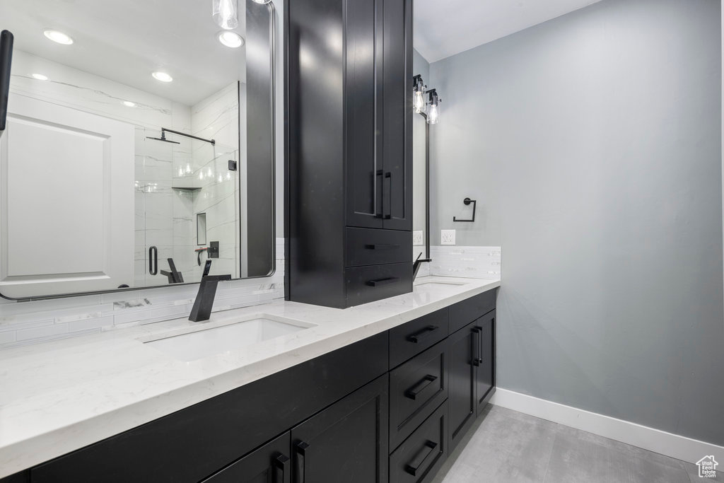 Bathroom featuring a sink, a stall shower, decorative backsplash, double vanity, and baseboards